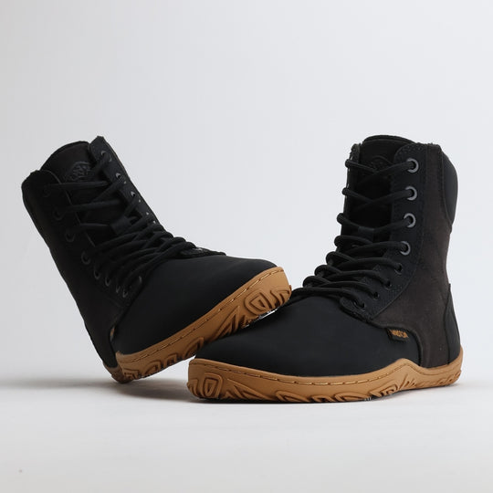 Black barefoot winter boot with the sole leaning against the toe box on a light gray background.