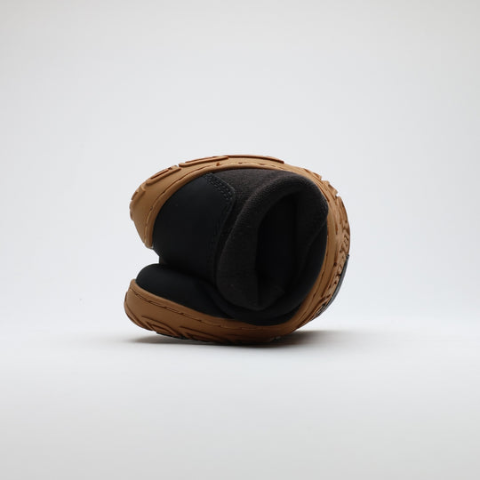 Black barefoot winter boot folded to demonstrate its thin and flexible sole on a light gray background.