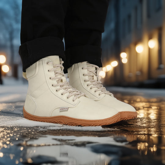 Off white barefoot winter boots worn while standing in an evening city setting, highlighting the sleek design, flexibility, and natural movement style.