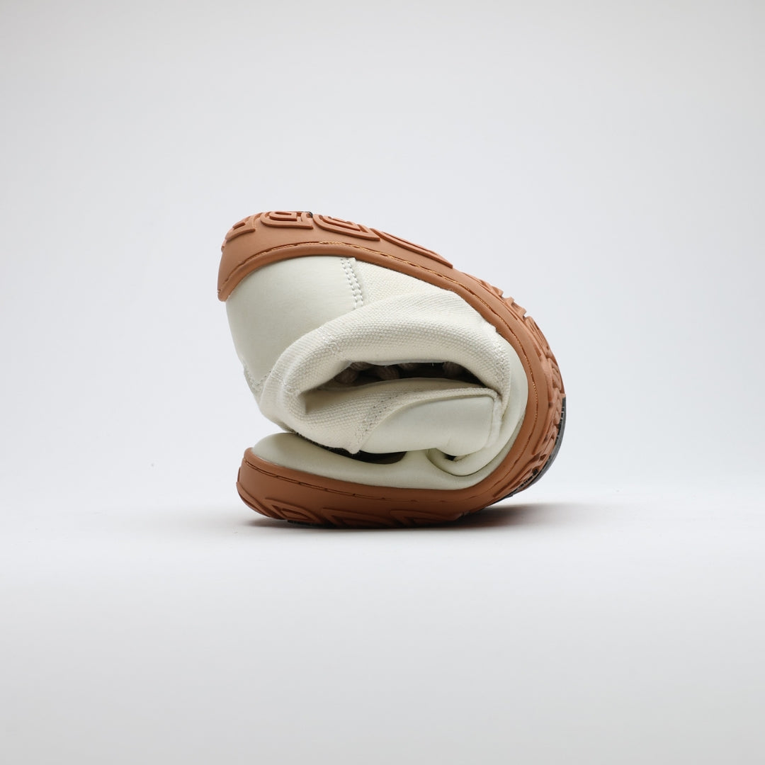 Off white barefoot winter boot folded to demonstrate its thin and flexible sole on a light gray background.