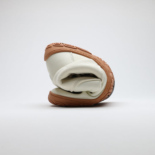 Off white barefoot winter boot folded to demonstrate its thin and flexible sole on a light gray background.