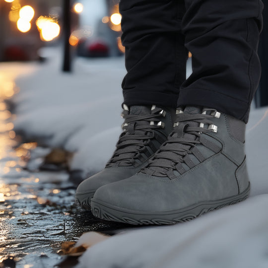 Frost gray barefoot hiking boots shown from a front angle in an evening city setting, highlighting the sleek waterproof design and natural movement style.
