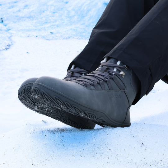 Frost gray barefoot hiking boots worn outdoors on a snowy hill in daylight, shown while sitting, highlighting comfort, warmth, and natural movement in winter conditions.