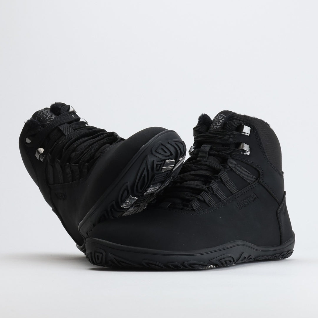 Black barefoot hiking boot with the sole leaning against the toe box on a light gray background.