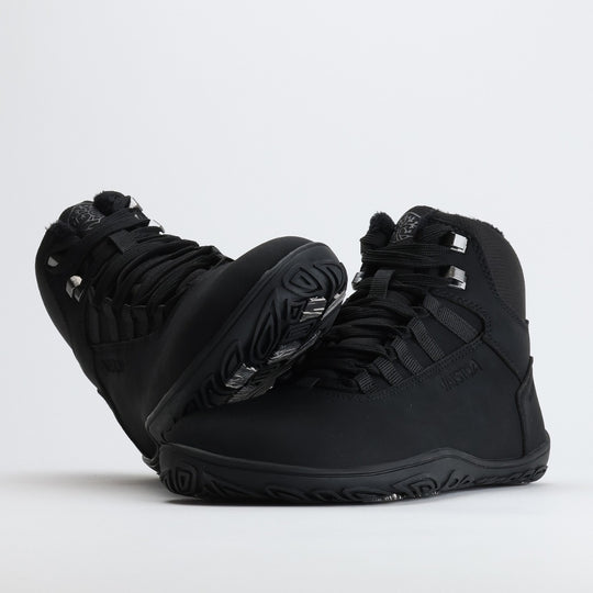 Black barefoot hiking boot with the sole leaning against the toe box on a light gray background.