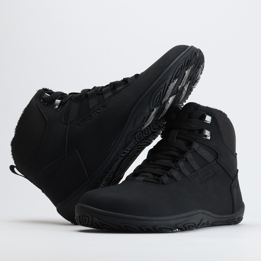Black barefoot hiking boot with the sole resting against the upper, showing visible grip zones on the winter sole.