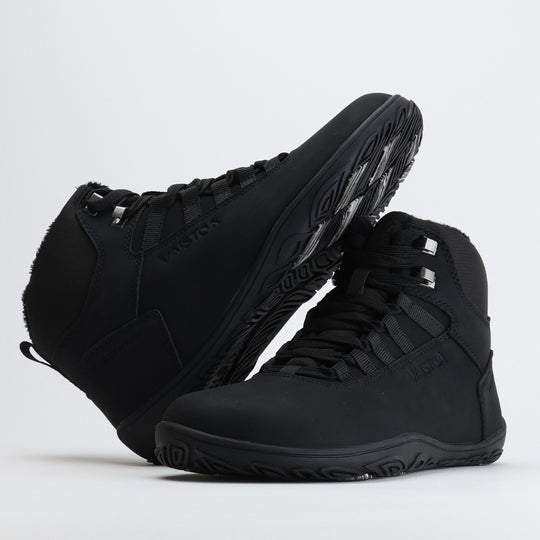 Black barefoot hiking boot with the sole resting against the upper, showing visible grip zones on the winter sole.