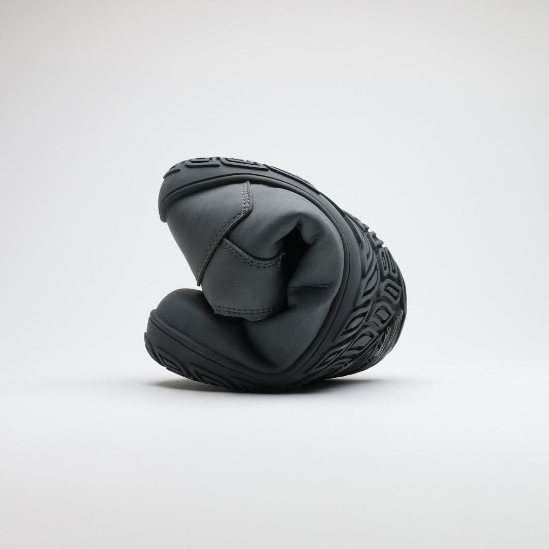 Frost gray barefoot hiking boot folded to demonstrate its thin and flexible sole on a light gray background.