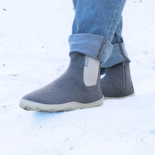 Pearl grey barefoot winter felt Chelsea boots worn with blue jeans in a snowy winter setting, shown from a front angle to highlight their cozy felt upper, natural movement, and Scandinavian minimalist design.