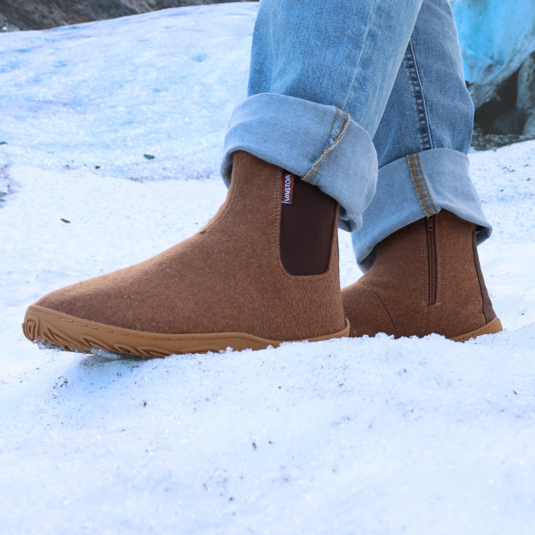 Roasted almond barefoot winter felt Chelsea boots worn with blue jeans in a snowy setting, shown from the front to highlight their warm felt material, flexible sole, and natural barefoot design.