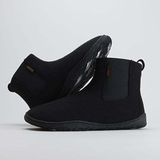 Velvet black barefoot winter felt Chelsea boots shown from the lateral side, with one boot leaning against the other to display the natural foot shape and flexible construction.