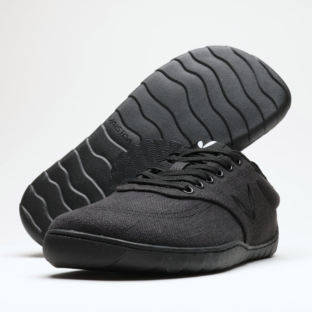 Vaistoa Huoleton barefoot hemp sneakers – soft black, studio shot of the pair, one shoe on its side showing the wave pattern of the Vaistoa Aalto outsole and the other standing sideways in front, light background
