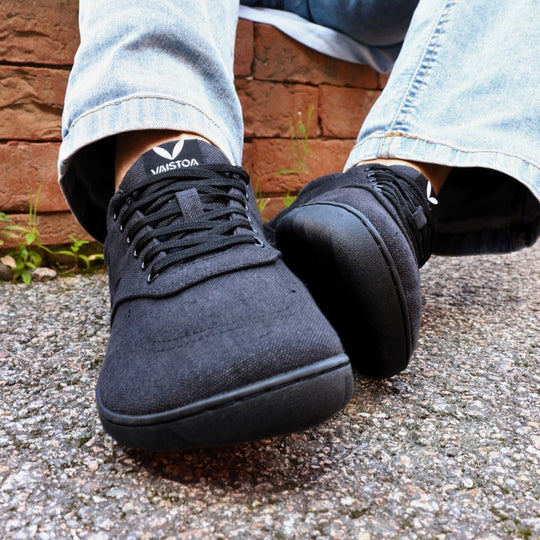 Vaistoa Huoleton barefoot hemp sneakers – soft black, close-up of the shoes worn on a gravel path, light blue jeans and Vaistoa socks visible