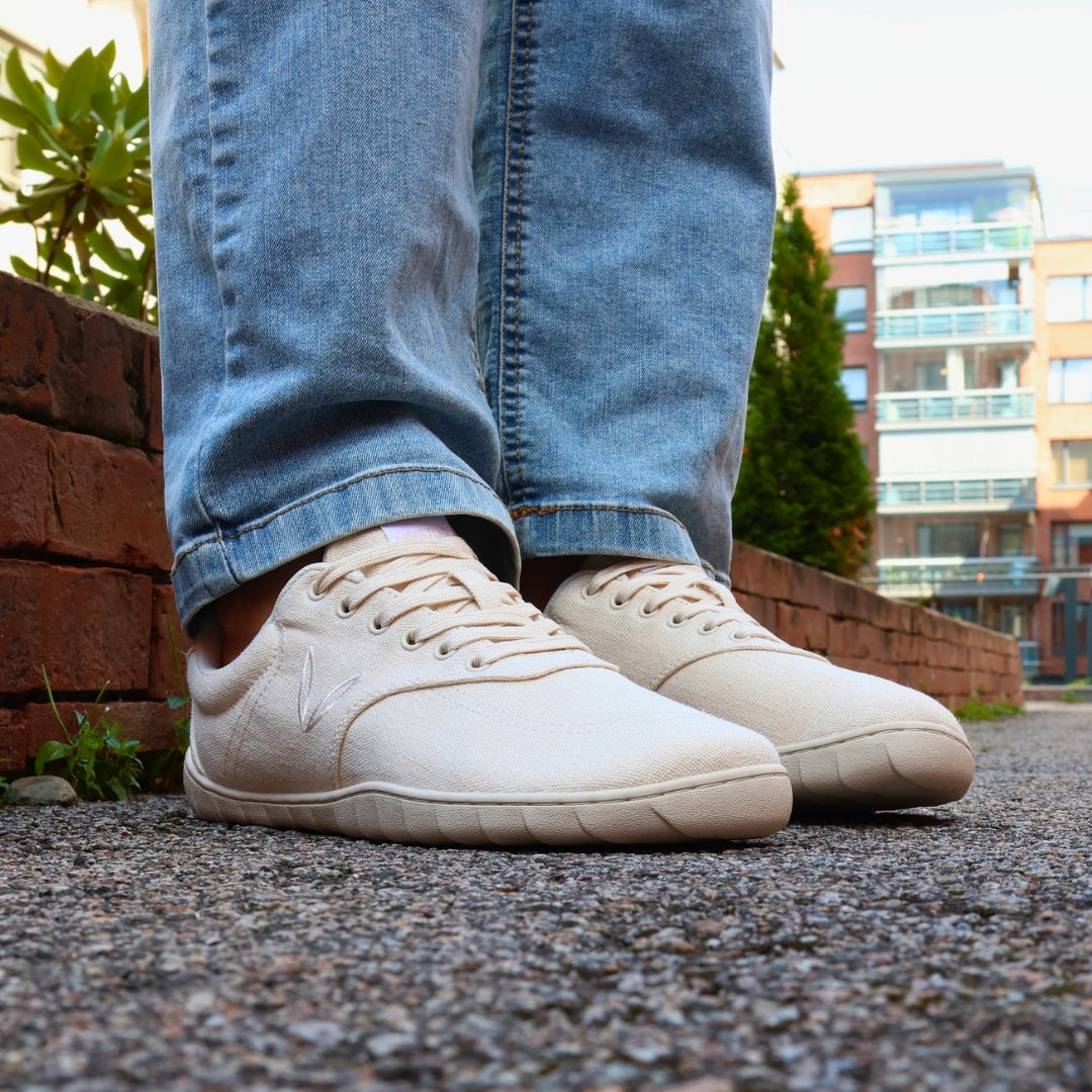 Vaistoa Huoleton barefoot hemp sneakers – natural hemp, shoes worn on a gravel path with blue jeans, red brick wall and apartment building in the background