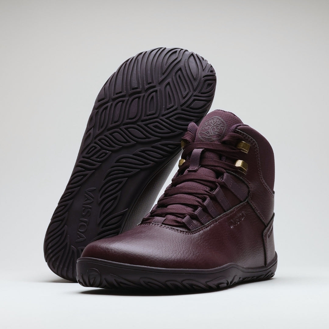 Vaistoa Uoma 2 barefoot trekking boots plum red – two boots on a studio background, one lying on its side with the leaf-patterned outsole facing the camera and the other standing at a front three-quarter angle