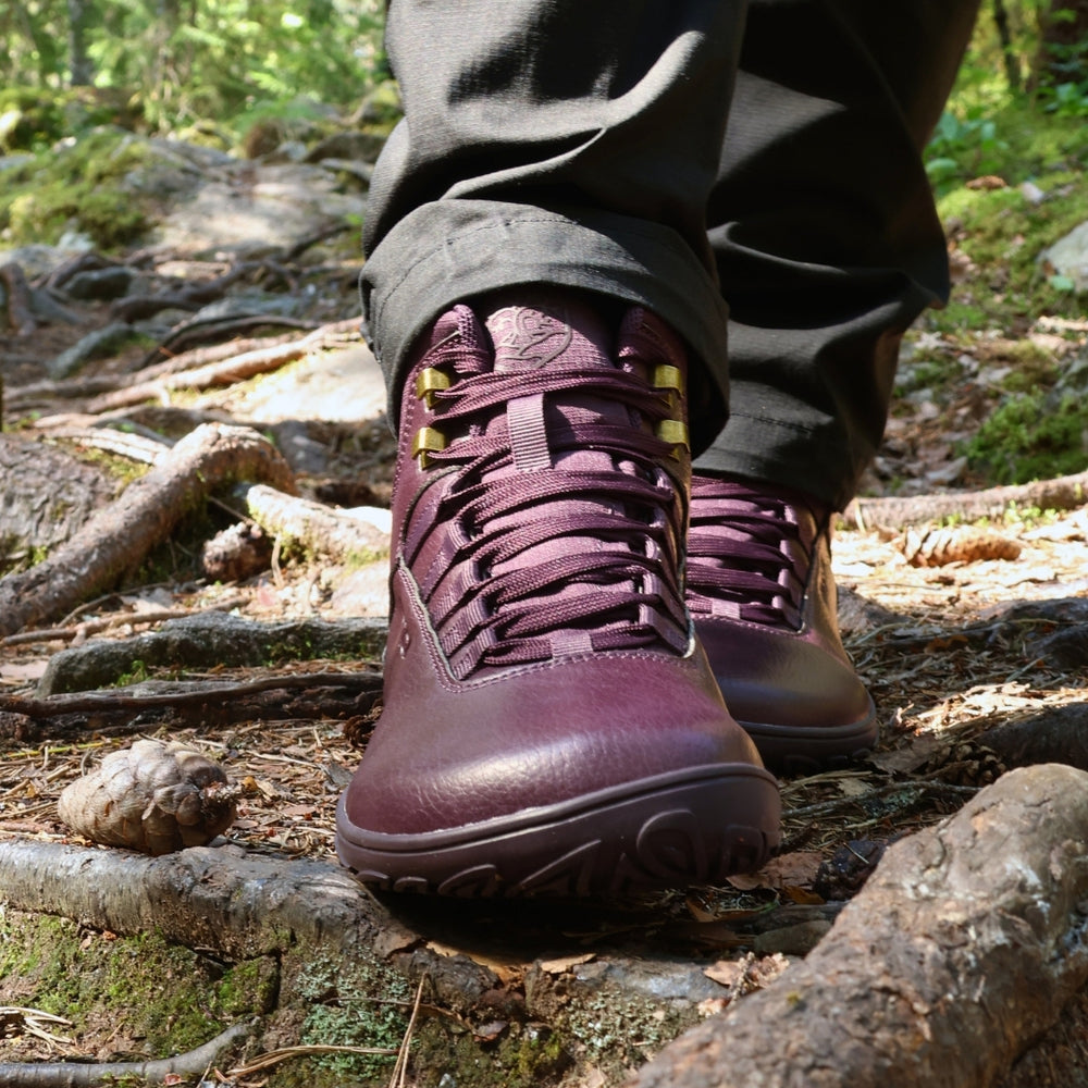 Vaistoa Uoma 2 barefoot trekking boots plum red – close-up of the boots being worn, the wearer standing on a root-covered forest floor, seen from the front at a low angle