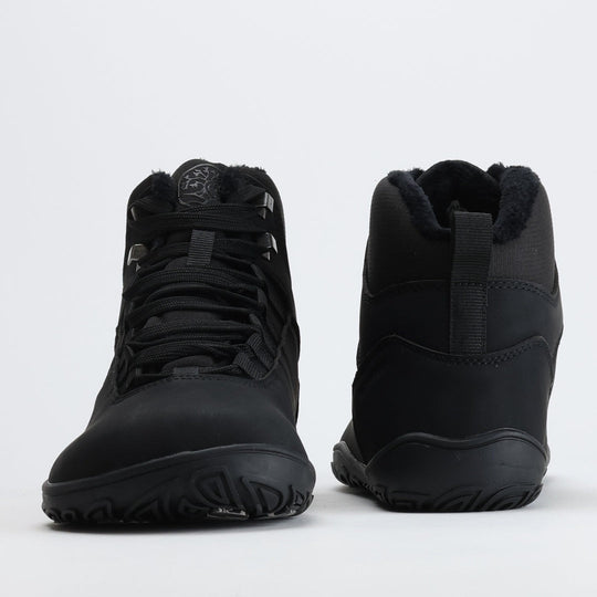 Noenmusta Vaistoa Uoma Talvi 3 -paljasjalkavaelluskenkäpari kuvattuna edestä ja takaa. Kuvassa näkyy leveä varvastila ja lämmin karvavuori.