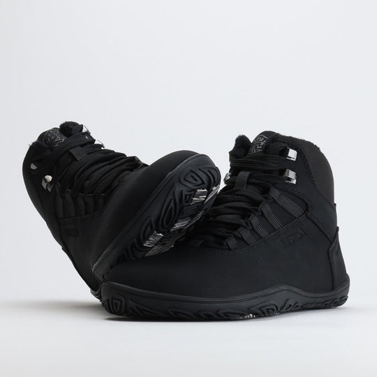 Noenmusta Vaistoa Uoma Talvi 3 -kenkäpari, jossa toinen kenkä nojaa toisen varvastilaan. Kuvassa korostuu leveä anatominen varvastila ja pitävä pohja.