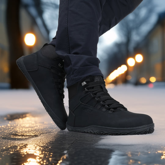 Black barefoot hiking boots in an evening city scene, shown from the side while taking a step, emphasizing flexibility and natural movement.