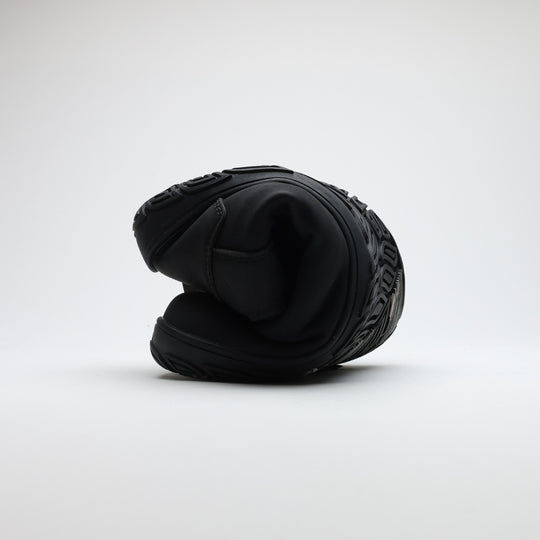 Black barefoot hiking boot folded to demonstrate its thin and flexible sole on a light gray background.