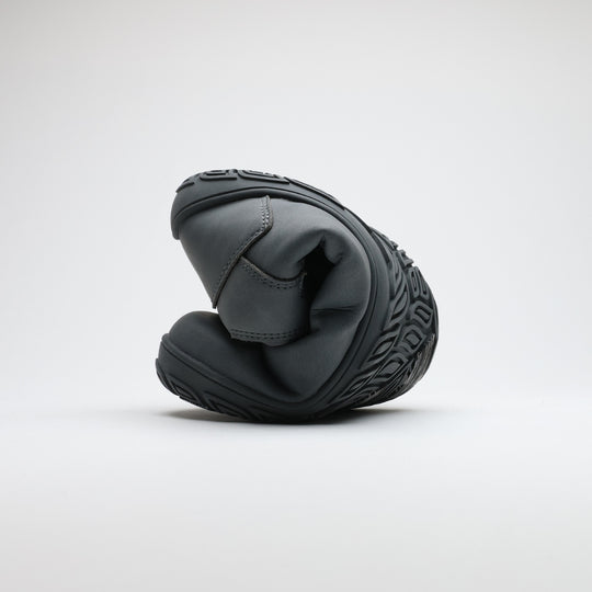 Frost gray barefoot hiking boot folded to demonstrate its thin and flexible sole on a light gray background.