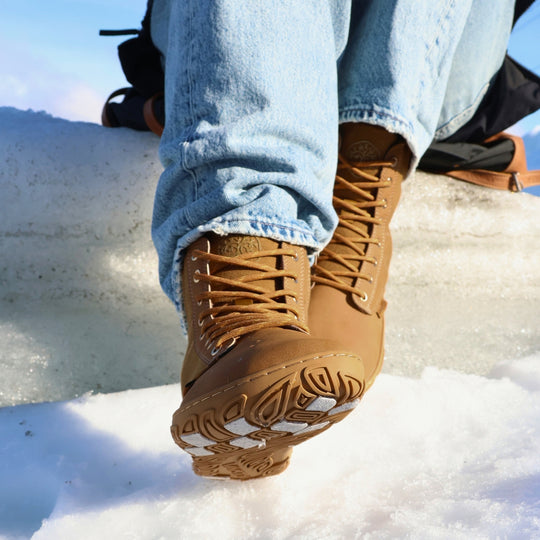 Vaistoa Hurmos 3 casual winter barefoot boots – lifestyle photo: a step on snowy ice with blue jeans, the outsole and light grip pads of the lifted shoe visible
