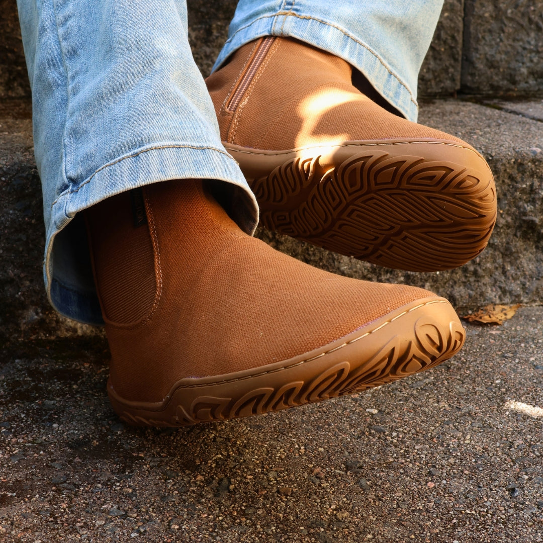Vaistoa Kajo 2 barefoot chelsea boots – almond brown shoes worn on foot on steps with one outsole towards the camera, light jeans
