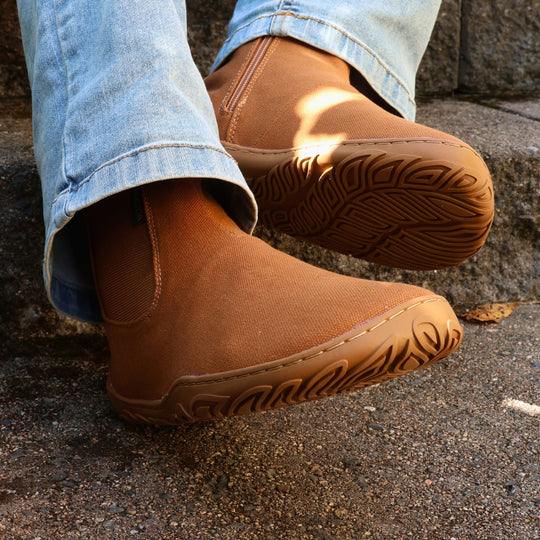 Vaistoa Kajo 2 barefoot chelsea boots – almond brown shoes worn on foot on steps with one outsole towards the camera, light jeans