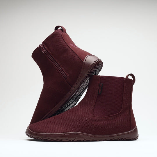 Vaistoa Kajo 2 barefoot chelsea boots – burgundy pair with one shoe on its side showing the zipper and the other standing in front showing the elastic panel against a light background