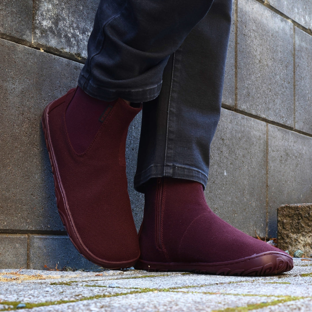 Vaistoa Kajo 2 barefoot chelsea boots – burgundy shoes worn on foot with one foot leaning against a concrete wall and the side zipper visible, black jeans