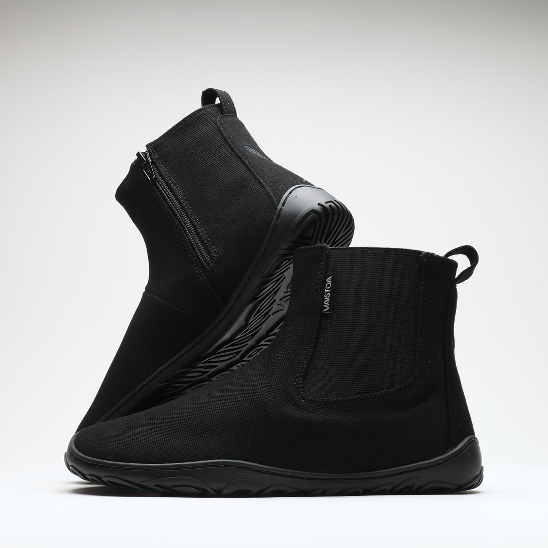 Vaistoa Kajo 2 barefoot chelsea boots – classic black pair with one shoe on its side showing the zipper and the other standing in front showing the elastic panel against a light background
