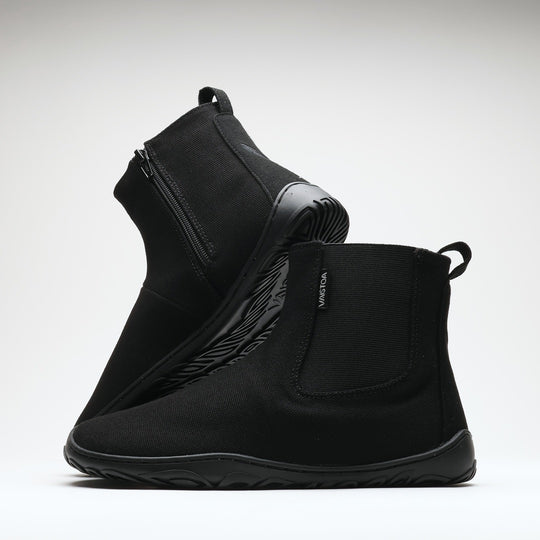 Vaistoa Kajo 2 barefoot chelsea boots – classic black pair with one shoe on its side showing the zipper and the other standing in front showing the elastic panel against a light background