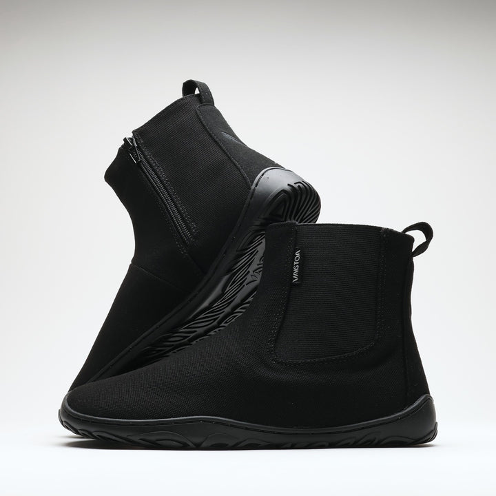 Vaistoa Kajo 2 barefoot chelsea boots – classic black pair with one shoe on its side showing the zipper and the other standing in front showing the elastic panel against a light background