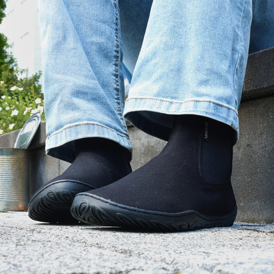 Vaistoa Kajo 2 barefoot chelsea boots – classic black shoes worn on foot on gravel in front of a concrete kerb, light jeans