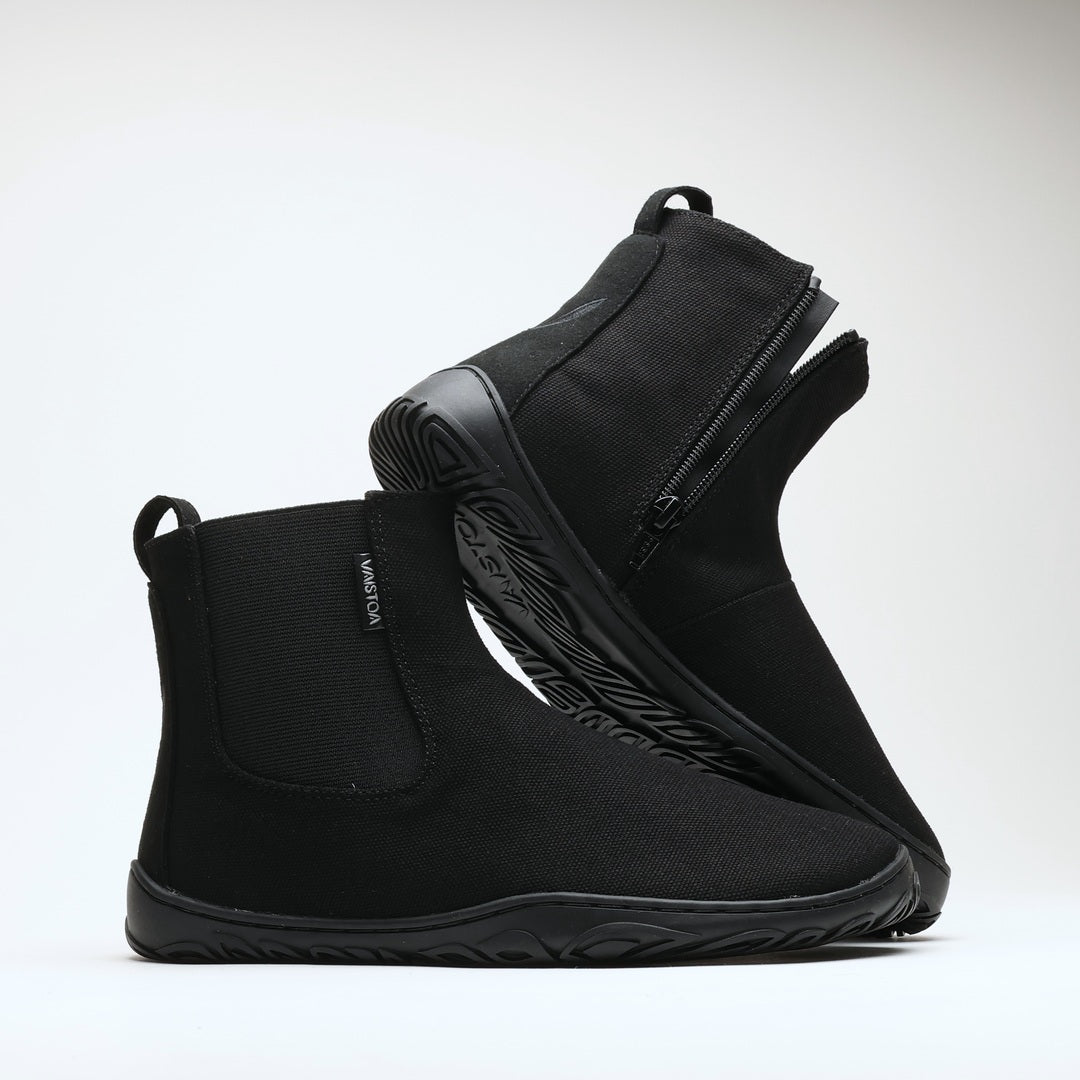 Vaistoa Kajo 2 barefoot chelsea boots – classic black pair with one shoe resting on the other so the side zipper and the edge of the outsole are visible against a light background