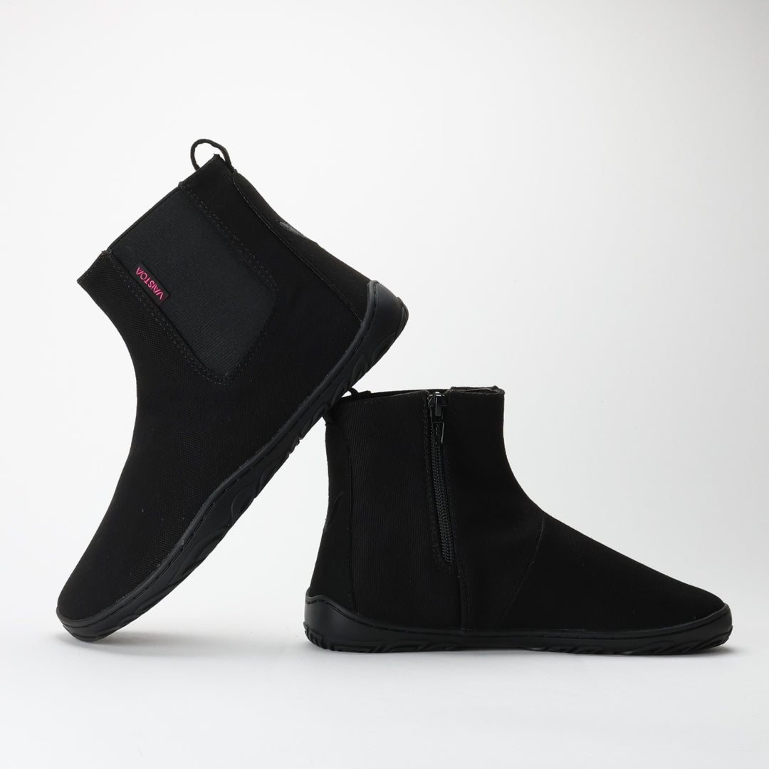 Vaistoa Kajo barefoot Chelsea boots – black, studio shot of the pair, one boot standing showing the elastic panel and the other in front showing the side zipper