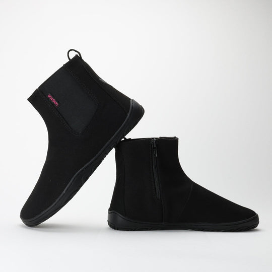 Vaistoa Kajo barefoot Chelsea boots – black, studio shot of the pair, one boot standing showing the elastic panel and the other in front showing the side zipper