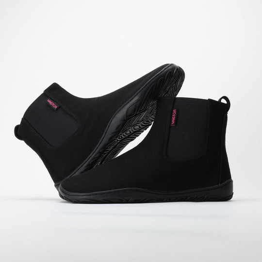 Vaistoa Kajo barefoot Chelsea boots – black, studio shot of the pair, the back boot tilted onto the front one, elastic side panel and the red Vaistoa label visible