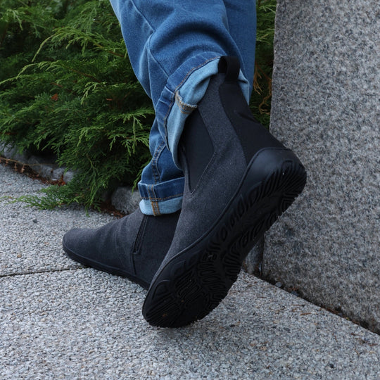 Vaistoa Kajo barefoot Chelsea boots – smoky stonewashed grey, boots worn with turned-up blue jeans, one foot resting against a granite wall so the outsole tread is visible