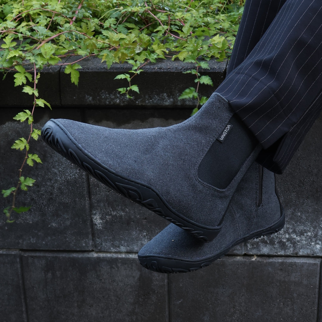 Vaistoa Kajo barefoot Chelsea boots – smoky stonewashed grey, boots worn with pinstripe suit trousers, one foot raised on a stone wall showing the side and sole of the boot