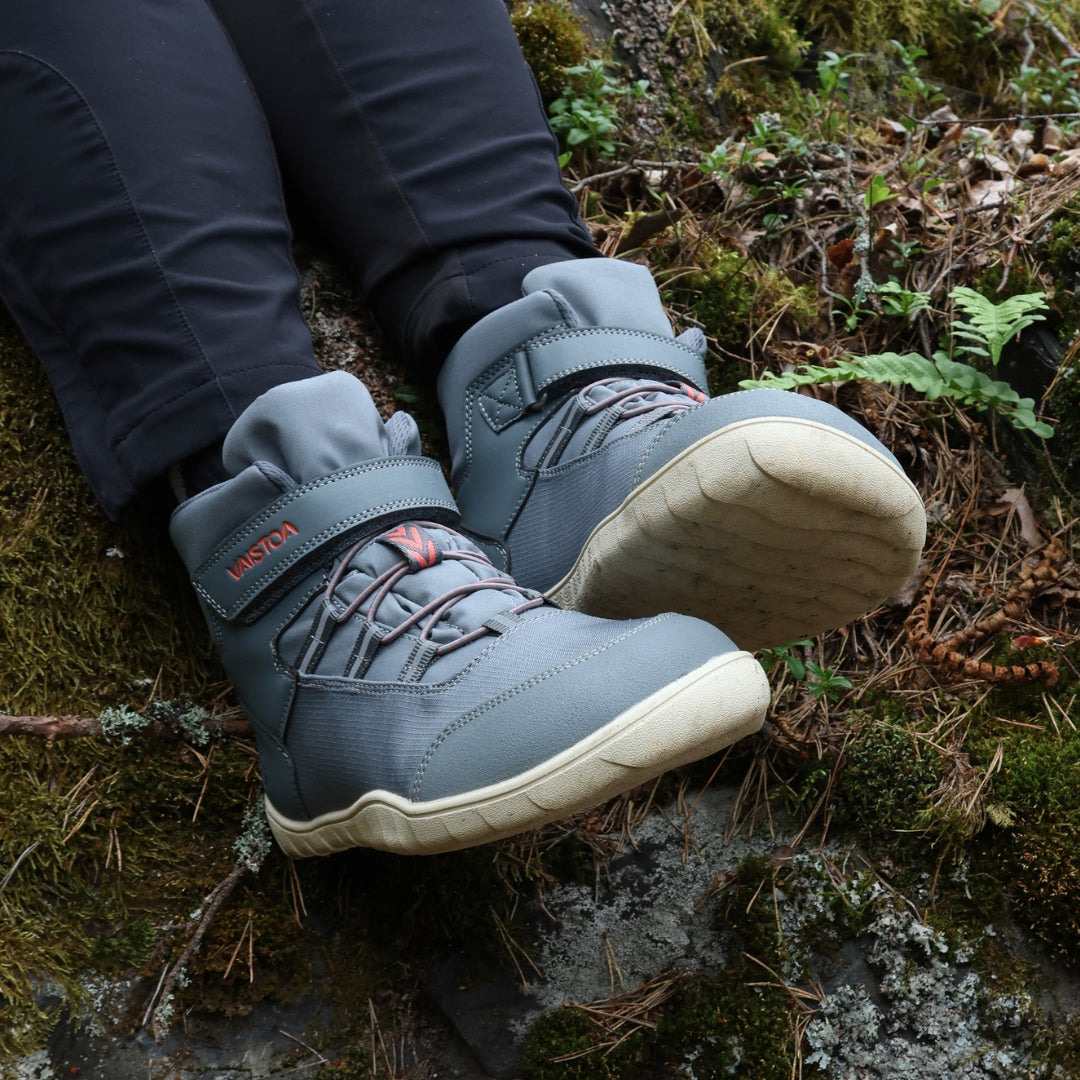 Vaistoa Kaste waterproof barefoot shoes for kids blue grey – worn shoes resting on a mossy rock, with the cream outsole of the right shoe facing the camera