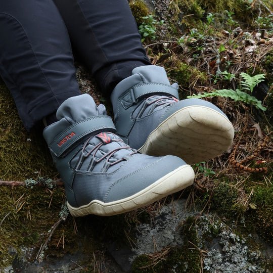 Vaistoa Kaste waterproof barefoot shoes for kids blue grey – worn shoes resting on a mossy rock, with the cream outsole of the right shoe facing the camera