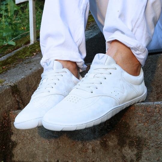 Vaistoa Katu 2 white barefoot sneakers in use – person standing outdoors on stairs on a summer day, wearing white jeans, pictured close-up.