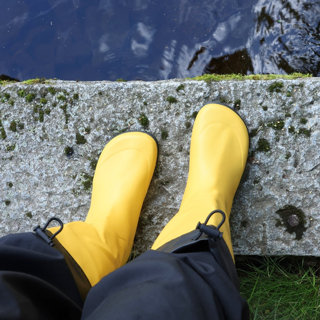 Vaistoa Katve 2 barefoot rubber boots yellow seen from above on the edge of a stone above the water