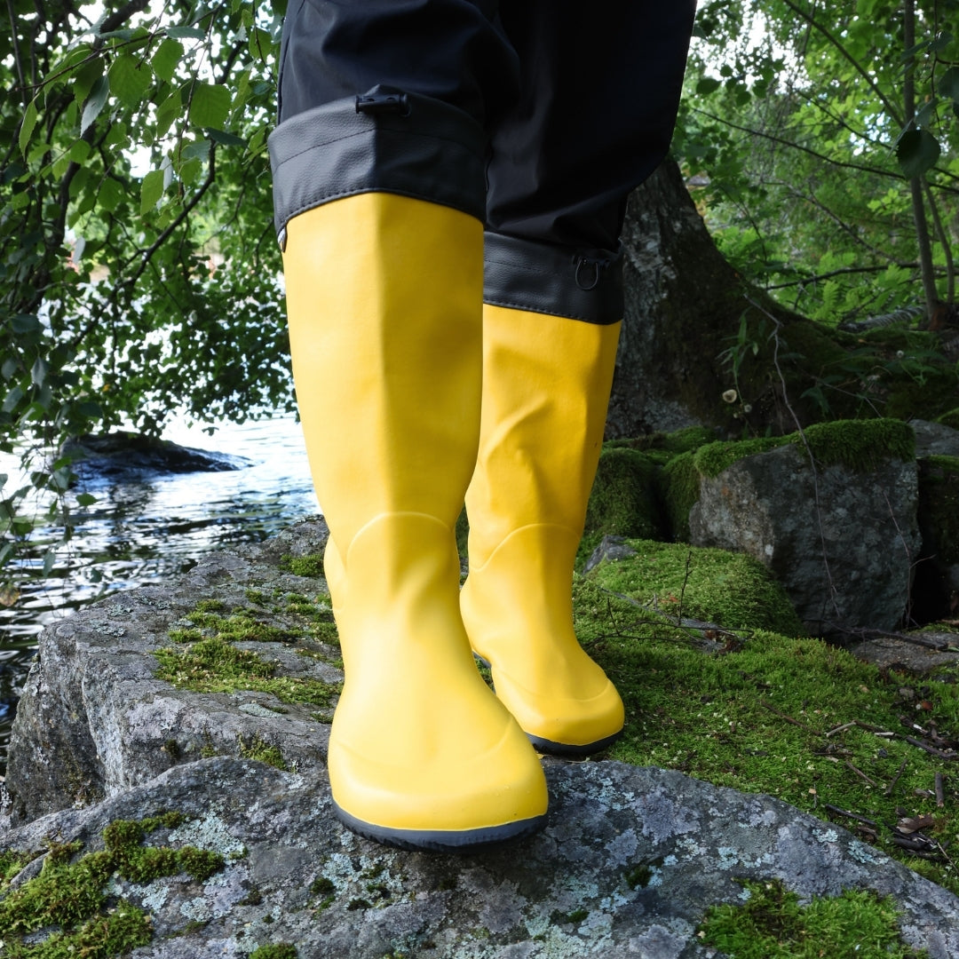 Vaistoa Katve 2 barefoot rubber boots yellow worn on a mossy rock at the water's edge
