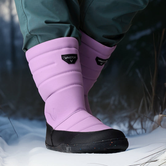 Vaistoa Kinos – lasten korkeavartiset paljasjalkakengät talveen, väri lila. Käyttökuva: etuviistosta kuvattuna sinisten housujen kanssa talviympäristössä.