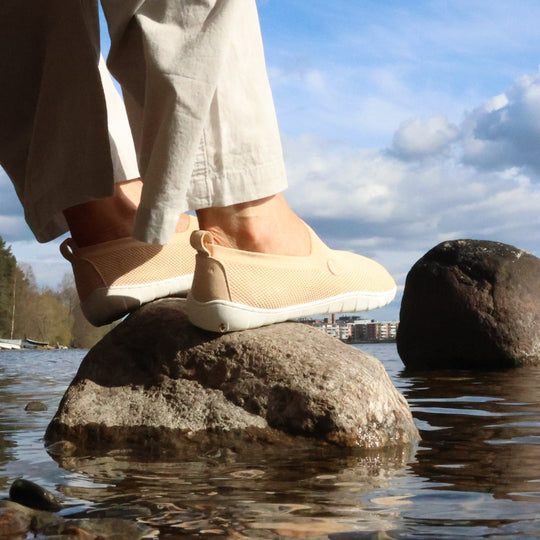 Vaistoa Lempeä 2 barefoot slip-on shoes peach – lifestyle photo, beige pants sitting by the lake