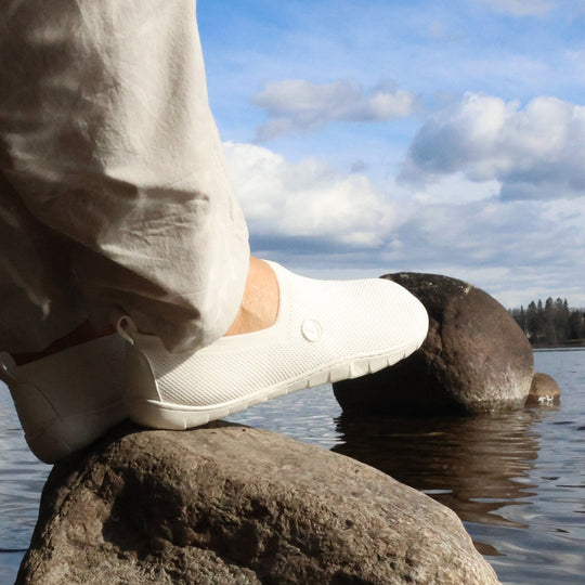 Vaistoa Lempeä 2 barefoot slip-on shoes white – lifestyle photo, beige pants sitting by the lake