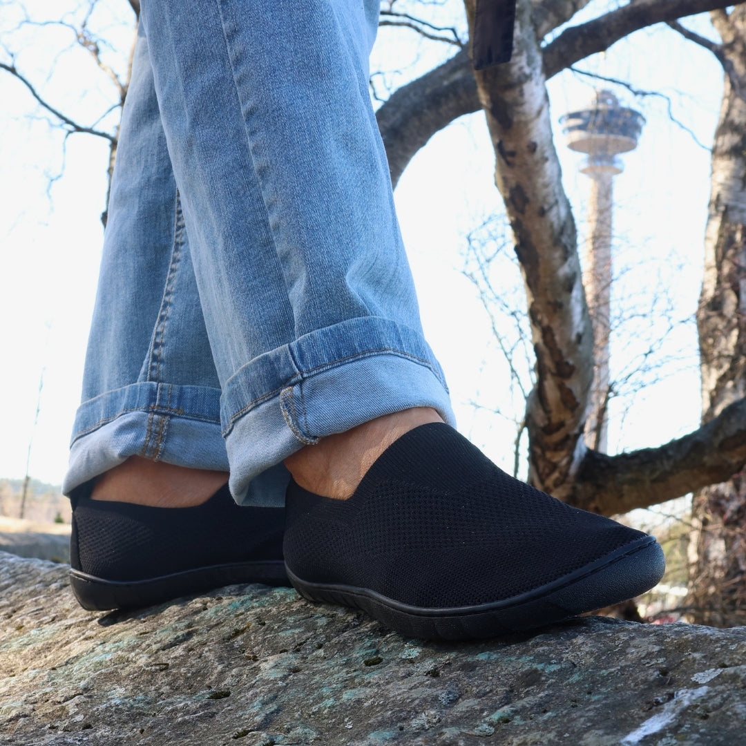 Vaistoa Lempeä 3 slip-on barefoot shoes – black shoes worn while standing on a rock, with jeans visible