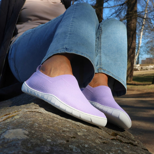 Vaistoa Lempeä 3 slip-on barefoot shoes – lavender shoes worn on feet while sitting on a rock, paired with blue jeans
